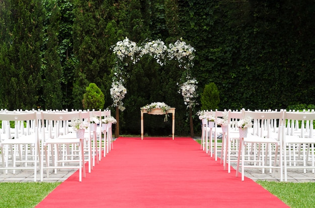 Foto decoração bonita da cerimônia de casamento, altar rústico decorado com flores de lírios, alstroemerias e crisântemos atrás da parede de hera, tapete vermelho com cadeiras brancas. conceito de dia do casamento.