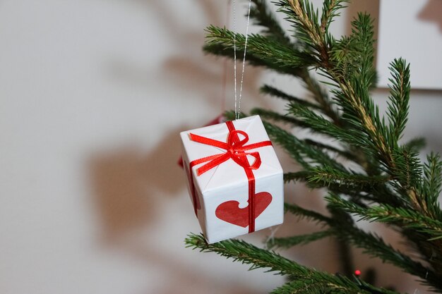 Decoração da árvore de Natal na forma de uma pequena caixa de presente de cor branca com uma fita vermelha