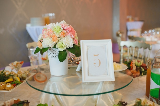 Decoração da mesa de convidados com um sinal 5 e flores em um vaso branco