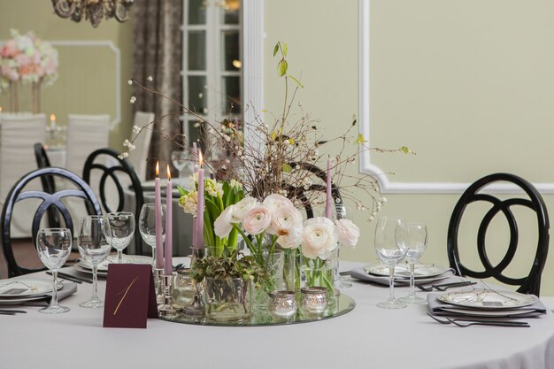 Decoração da mesa festiva no restaurante com velas, flores, peônias e botões de ouro, ramos