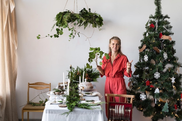 Decoração da sala de estar com uma mesa festiva para o Natal A menina decora a sala para o Ano Novo Árvore de Natal decorada no canto da sala