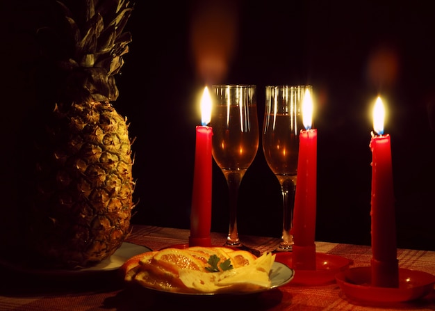 Decoração de abacaxi com três velas vermelhas acesas e taça de vinho