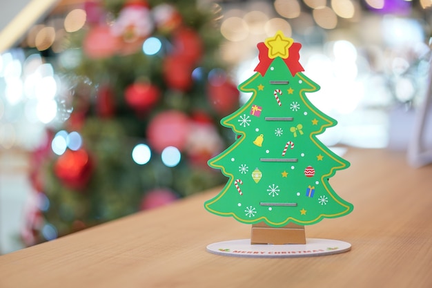 Decoração de artesanato de papel de árvore de Natal traseira na mesa de madeira com borrão de árvore de Natal grande atrás.