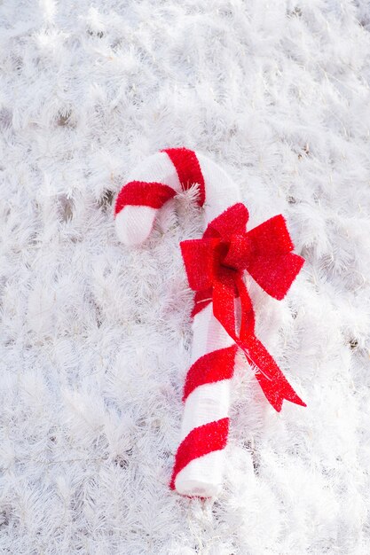 Decoração de bastão de doces de Natal com laço vermelho em fundo de agulha de abeto branco artificial. natal, ano novo, conceito de celebração de férias de inverno