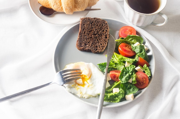 Decoração de configuração de mesa de primavera de manhã. salada no prato, ovo, xícara de café e croissant, tulipas frescas em um vaso no fundo de toalha de mesa branca limpa. ajuste de lugar de mesa de café da manhã na cor branca.