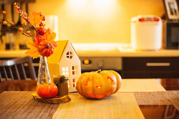 Decoração de cozinha para o Halloween: casa de papelão luminosa, vela, folhas de outono, caqui, jack-o-lantern