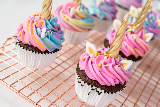 Decoração de cupcakes de unicórnio de chocolate com cobertura colorida de creme de manteiga e granulado.