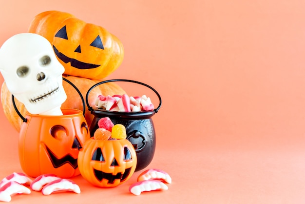 Decoração de feliz dia das bruxas. Bombons de abóbora, caldeirão, caveira e goma em fundo laranja.