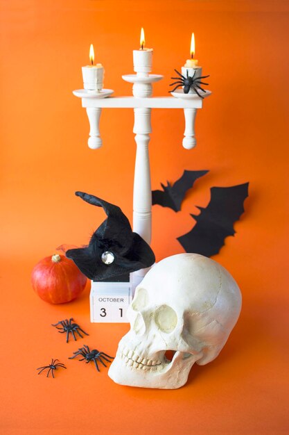 Decoração de Halloween com candelabro de crânio, velas, abóbora e morcegos em fundo laranja