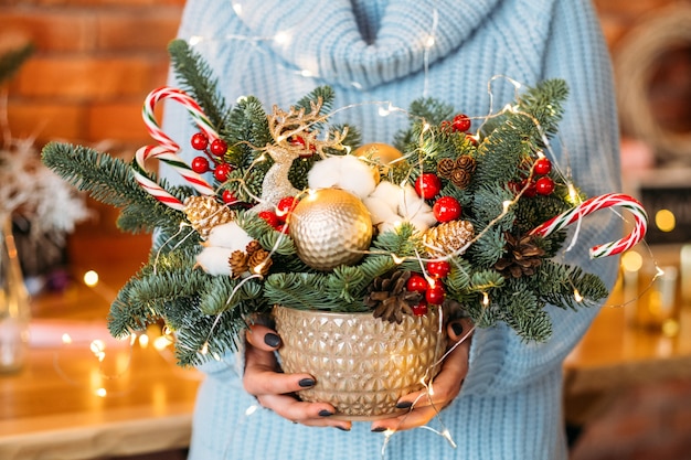 Decoração de Natal artesanal. senhora segurando a panela com galhos de árvore do abeto, bastões de doces e luzes de fada.