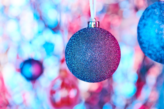 Decoração de natal azul coberta com pequenos brilhos de prata pendurados na frente da câmera em um fundo de Natal colorido formado por outras bolas de brinquedo