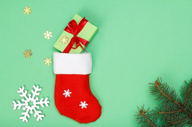 Decoração de Natal. Bota do Papai Noel, caixa de presente, galho de árvore do abeto e flocos de neve de brinquedo sobre fundo verde. Vista do topo. Conceito de cartão de Natal.