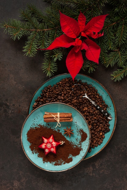 Decoração de Natal com galhos de pinheiro, poinsétia e grãos de café em um prato com paus de canela