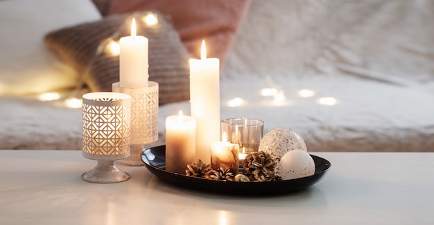Decoração de Natal com velas acesas na mesa branca contra o sofá com mantas e travesseiros.