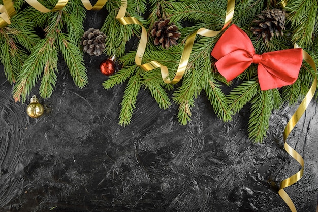 Decoração de Natal. Galho de árvore do abeto com bolas, presentes, pinha e arcos em uma superfície de madeira preta