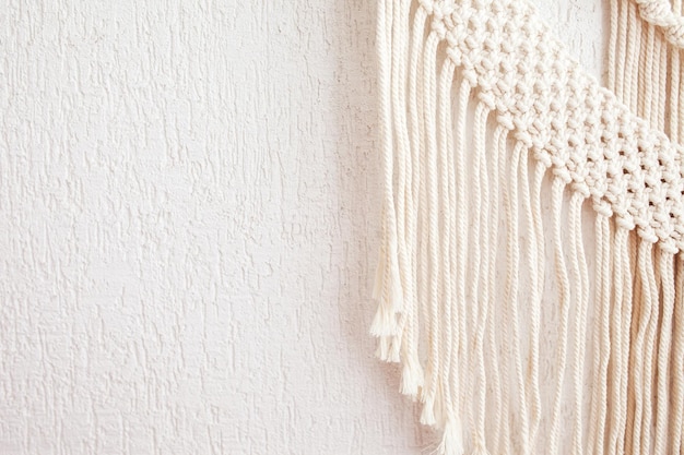 Foto decoração de parede de algodão macramê 100 artesanal com vara de madeira pendurada em uma parede branca trança de macramê e fios de algodão passatempo feminino eco amigável moderno conceito de decoração natural