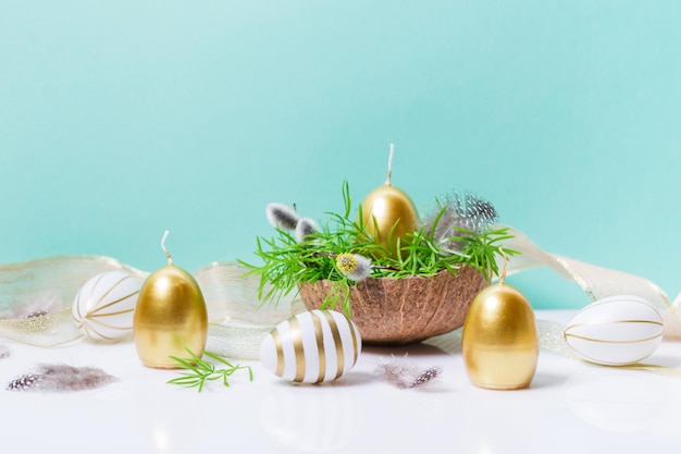 Decoração de páscoa com ovos e velas douradas e fitas com elementos botânicos naturais sobre fundo azul