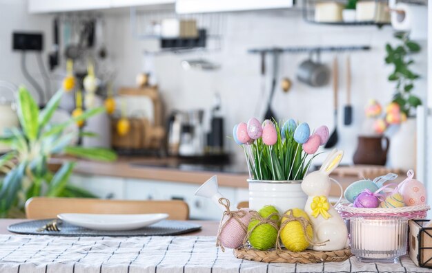 Decoração de Páscoa de ovos coloridos em uma cesta e um coelho na mesa da cozinha em estilo rústico Interior festivo de uma casa de campo