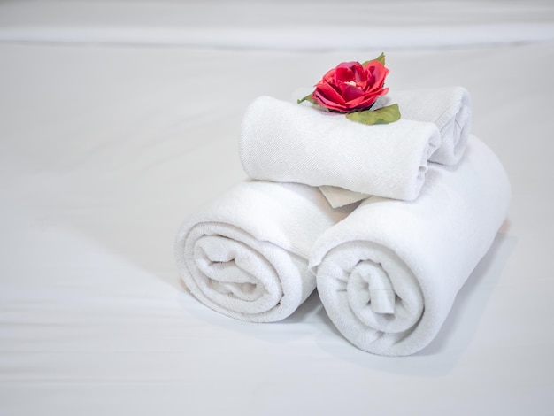 Decoração de toalhas limpas brancas com flor vermelha na cama limpa branca no quarto de hotel