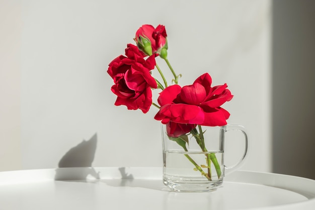 Decoração, interior. lindas rosas vermelhas em um copo de vidro na mesa branca