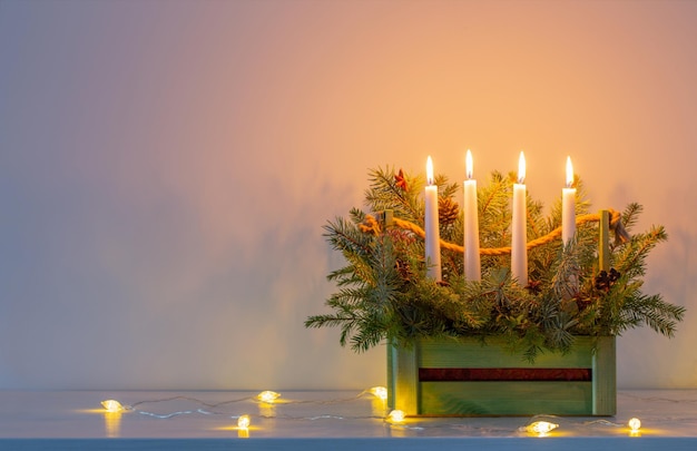 Decoración de adviento con ramas de abeto y cuatro velas encendidas en cesta de madera sobre fondo blanco.