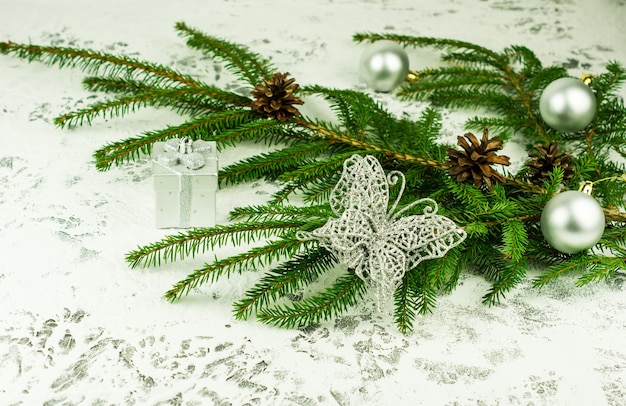 Decoración de año nuevo de la casa con una rama verde de abeto con conos con bolas brillantes y mariposa plateada calada. Fondo de nieve blanca.