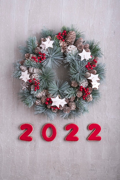 Decoración de año nuevo con números 2022. Corona de Navidad. Patrón de vacaciones de invierno. Pared gris claro en el fondo. Marco vertical.