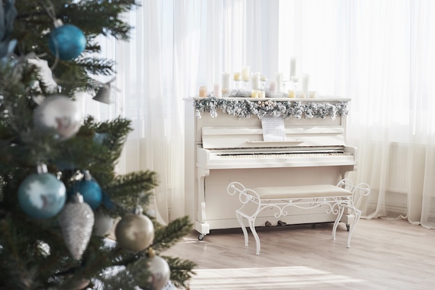 Decoración de año nuevo. Árbol de navidad cerca de piano blanco en la ventana