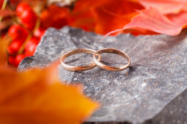 Decoración de boda. Hojas rojas en piedra desgastada con anillos de boda