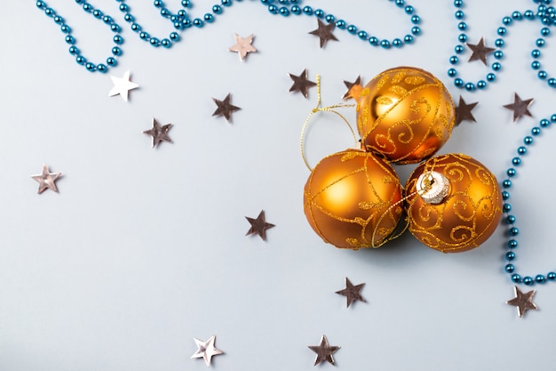 Decoración de bolas de Navidad brillantes doradas sobre fondo azul con estrellas plateadas y cuentas