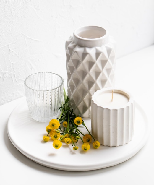 Foto decoración casera blanca con flores amarillas, jarrón de cerámica, velas y vidrio en bandeja