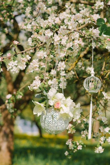 Decoración colgante en forma de jarrón plateado con flores colgando de una rama floreciente de un manzano en la primavera en el jardín