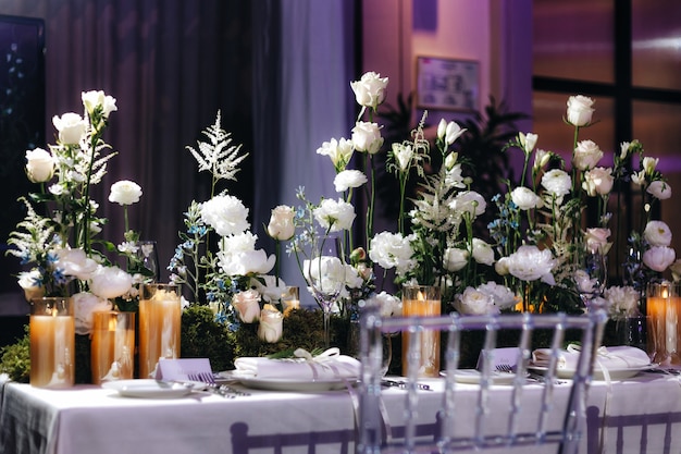 Foto decoración de diseño de mesa de boda romántica con grandes ramos de flores exuberantes que incluyen rosas blancas, ranúnculos, ranúnculos persas, orquídeas blancas y velas. foto de alta calidad