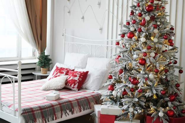 Decoración del dormitorio de Navidad Cerca de la ventana hay una cama doble y un árbol de Navidad con regalos