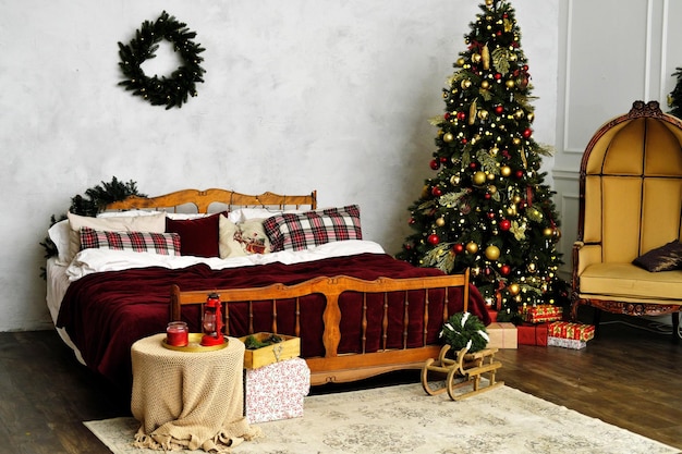 Decoración del dormitorio de Navidad Una gran cama de madera con una colcha roja y almohadas a cuadros y un árbol de Navidad en la esquina de la habitación