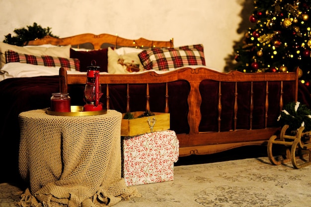 Decoración del dormitorio de Navidad Una gran cama de madera con una colcha roja y almohadas a cuadros y un árbol de Navidad en la esquina de la habitación