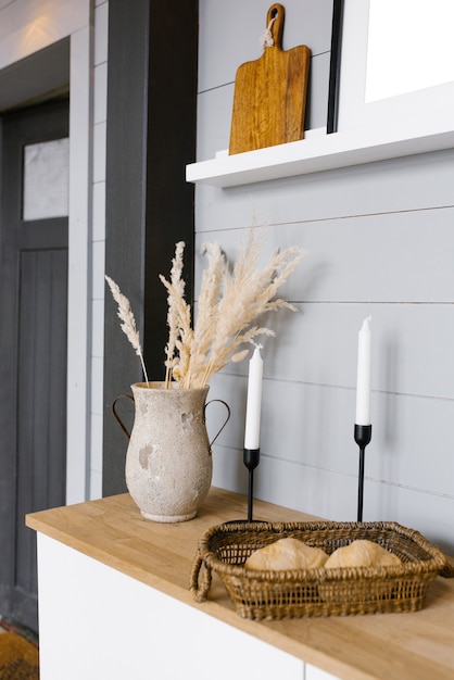 Decoración escandinava moderna con estilo minimalista en la cocina. Flores secas en un jarrón, velas blancas sobre candelabros negros y pan en una canasta