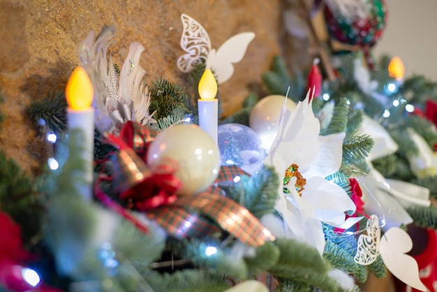 Decoración festiva de una guirnalda de árbol de Navidad con luces bombillas incandescentes juguetes arcos zapatos de punto bolas flor de pascua flores velas en una chimenea de piedra primer plano enfoque selectivo efecto borroso