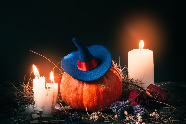 Decoración festiva de Halloween con calabaza naranja con sombrero de bruja, velas, rosas y heno seco.