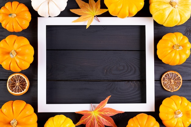 Decoración de fondo otoñal de hojas de arce y calabazas con marco de fotos en madera negra