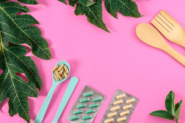 Foto decoración de fondo rosa con complementos dietéticos con equipamiento y hoja verde. medicina cuchara y suplementos dietéticos aislado sobre fondo rosa.