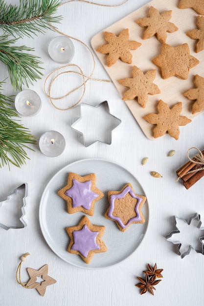 Decoración de galletas de jengibre con glaseado violeta sobre mesa de madera blanca con cortadores y velas