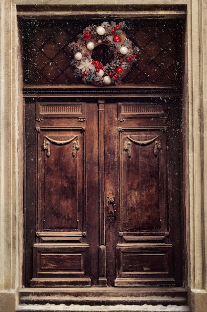 Decoración de la guirnalda de Navidad en la puerta para las vacaciones de invierno. Entrada de casa de madera marrón antigua decorada para Navidad. Diseño de estilo vintage