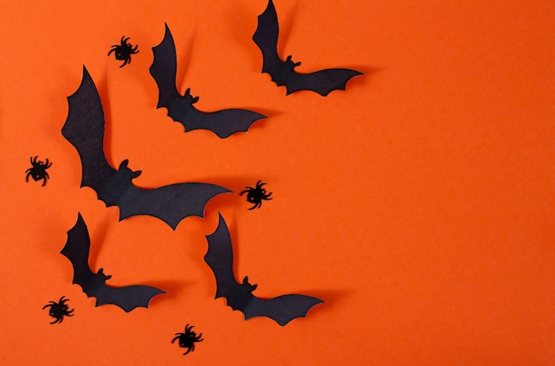 Decoración de Halloween con arañas y murciélagos de papel negro volando sobre fondo naranja