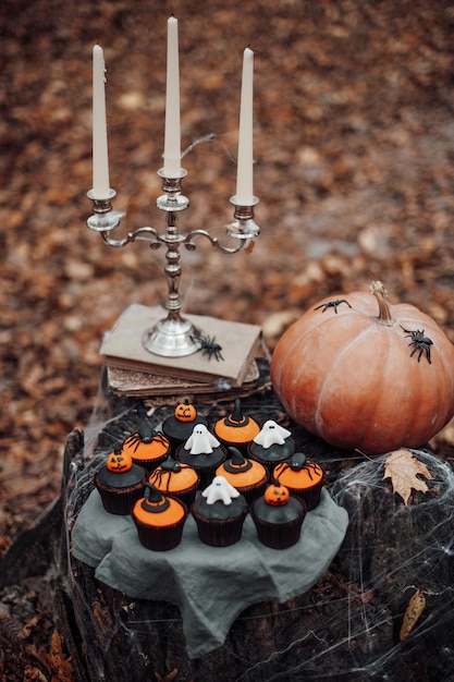 Decoración de Halloween con calabaza grande y dulces horribles en el viejo tocón de árbol Cupcakes con arañas arrastrándose sobre telaraña fantasmas espeluznantes misterioso sombrero negro y linterna jack en colores naranja