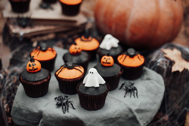 Decoración de Halloween con calabaza grande y dulces horribles en el viejo tocón de árbol Cupcakes con arañas arrastrándose sobre telaraña fantasmas espeluznantes misterioso sombrero negro y linterna jack en colores naranja