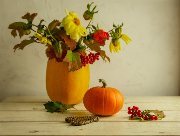 Decoración para halloween un jarrón de calabaza con flores y hojas de otoño y una pequeña calabaza naranja