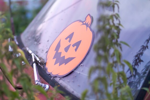 Decoración de Halloween en el viejo coche oxidado en arbustos de ortigas silvestres. Decoración de calabaza de papel naranja al aire libre.