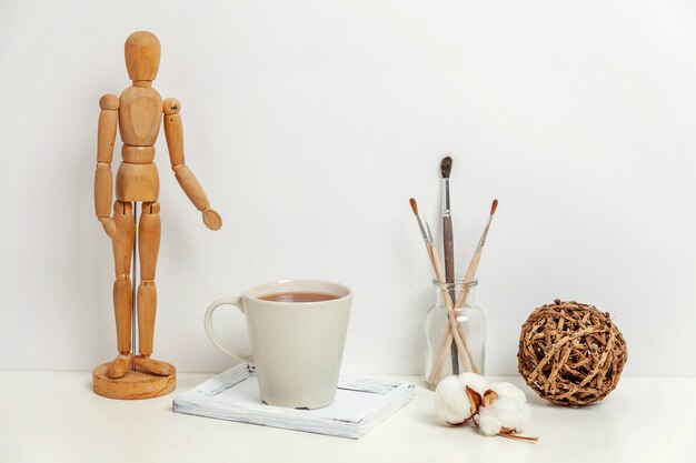 Decoración del hogar u oficina con taza de café de maniquí cerca de la pared blanca. El artista del lugar de trabajo interior del minimalismo suministra el fondo de la decoración. Concepto de espacio de trabajo de estilo escandinavo Hygge. Copia espacio maqueta