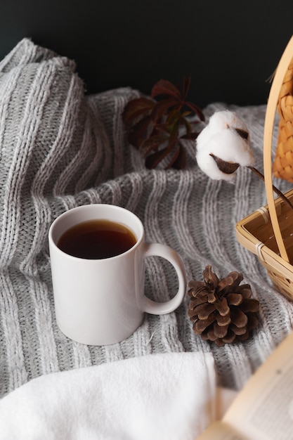 Decoración hogareña acogedora con un ambiente cálido. Taza blanca con té caliente y ropa de punto